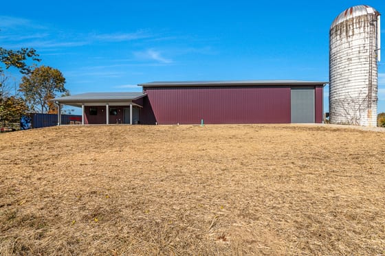 The full length of the red pole barn in daylight, silo alongside it, across a strawed field