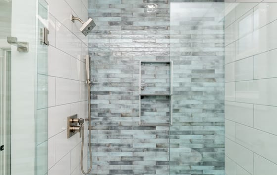 Glass-enclosed shower tiled in aqua and grey brick tile with a recessed niche and brushed nickel fittings
