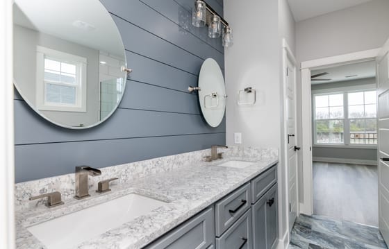 Double vanity seen along its length, with a round and an oval mirror on navy shiplap and a quartz top