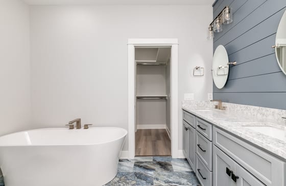 Primary bathroom with a freestanding oval tub, grey double vanity, navy shiplap, and patterned marble floor tile