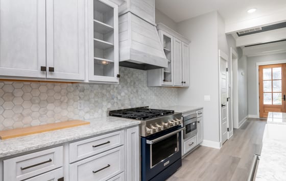 Range wall with a navy gas range, hexagonal tile backsplash, whitewashed hood surround, and marbled quartz counters