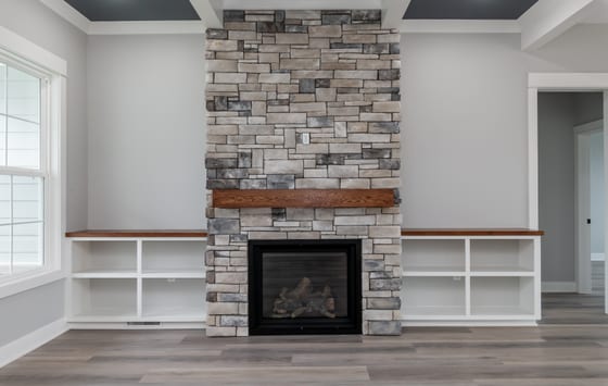 Stacked stone fireplace with a stained wood mantel, flanked by white built-in shelving with wood tops