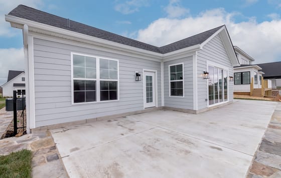 Rear elevation in grey lap siding, with a poured patio and sliding doors onto it