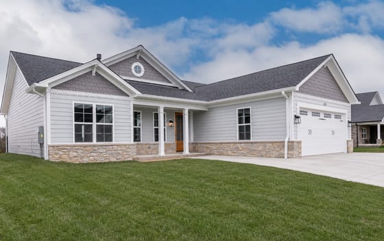 Craftsman-style custom home with grey lap siding, shake gables, and a stone-skirted front porch