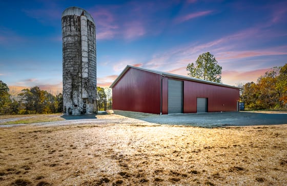 Red pole barn and an old concrete silo silhouetted against a violet and orange dusk sky